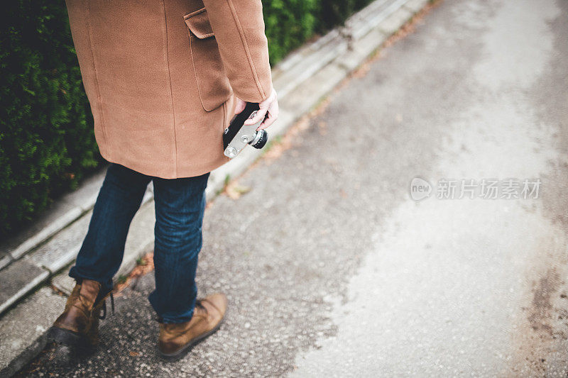 年轻的潮人带着复古的相机，穿着大衣从后面站在户外。