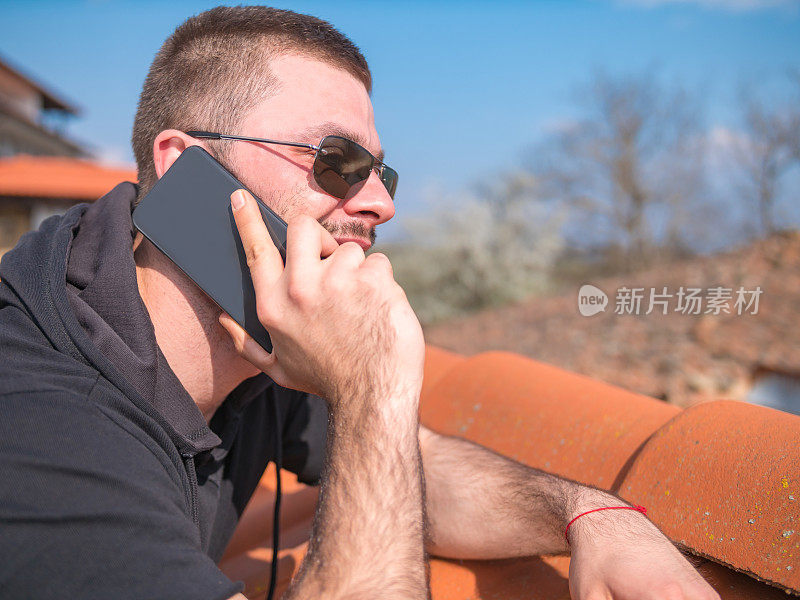 特写的男人靠在一堵石墙上，用他的智能手机说话