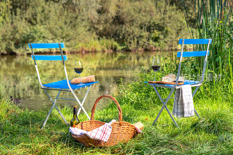 两张带野餐篮的折叠椅上放着奶酪和酒杯，可以在湖边吃早餐