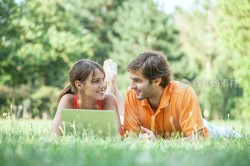 一对年轻夫妇躺在公园里用笔记本电脑