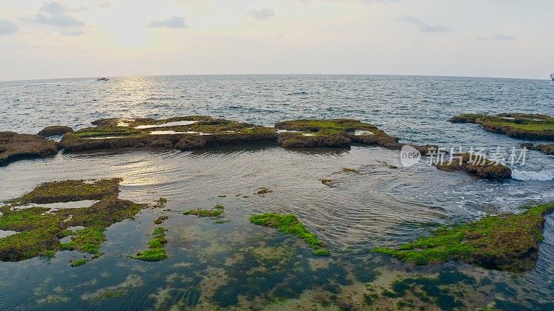 日落时的游船靠近布满苔藓的岩石海岸线