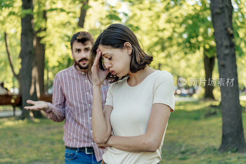 一对年轻夫妇在公园里吵架。年轻夫妇有一个夏天的一天争吵。站在公园外面，困惑的年轻女子打着手势，看着她的男朋友