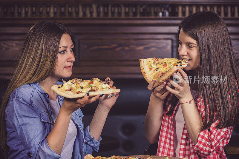 两个十几岁的女孩在餐厅享用美味的披萨