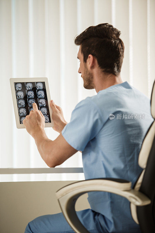 一名男性神经外科医生正在他的数码平板电脑上看脑瘤的核磁共振扫描图