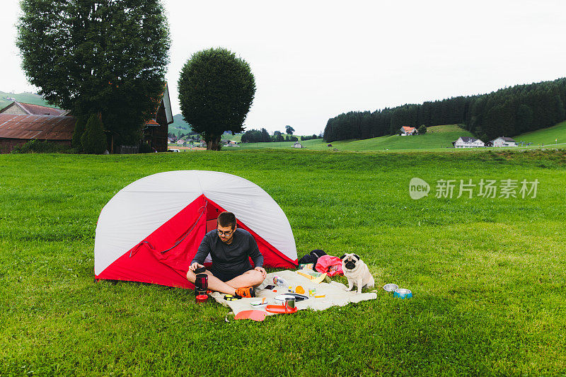 一名男子和一只狗在瑞士阿尔卑斯山的草地上搭帐篷度过了一个美好的夏日露营日