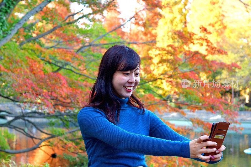 一名年轻的日本女子在东京井岛公园的秋叶下自拍