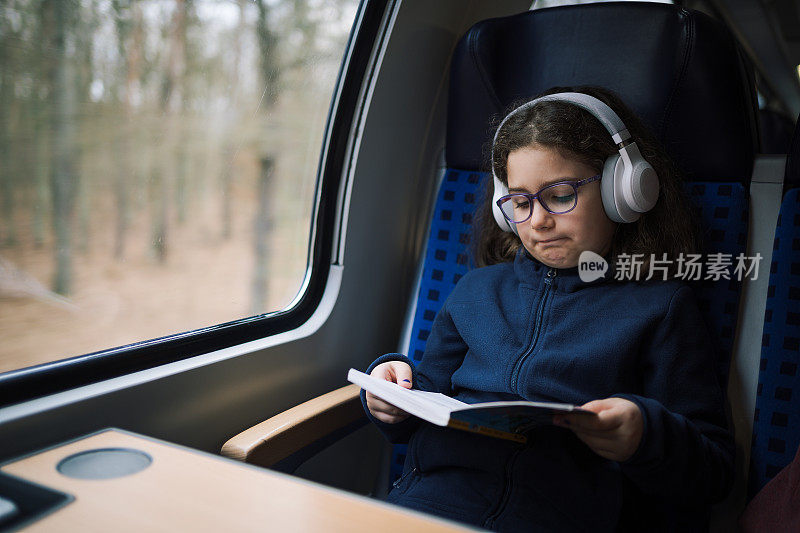可爱的小女孩坐火车在美丽的乡村旅行时看书和听音乐
