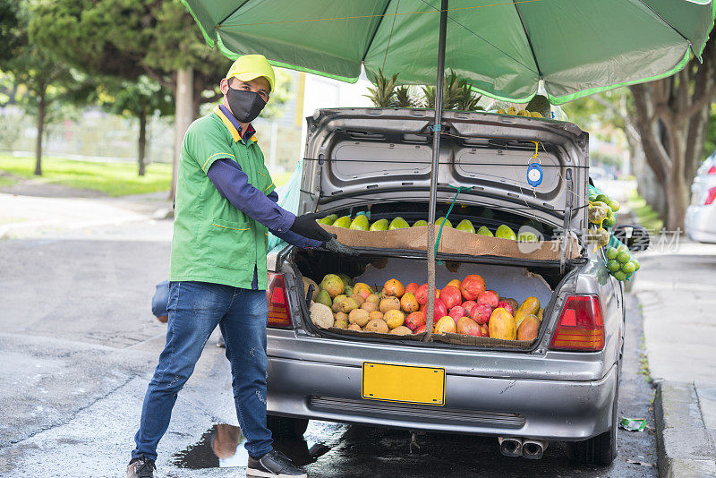 一名戴口罩的男子在一辆车里整理水果和蔬菜，以保护自己免受COVID-19病毒感染