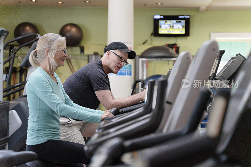 两个老年人，男人和女人一起在健身房里的自行车模拟器上健身