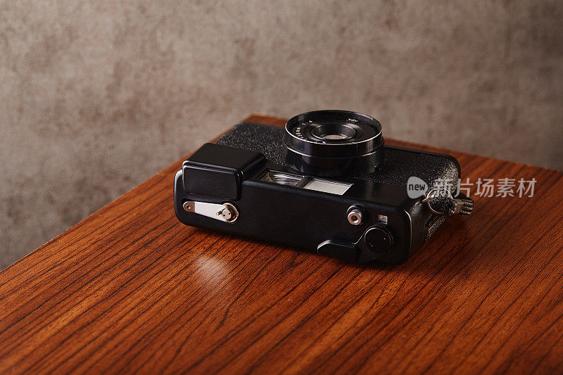 老式的模拟测距胶片相机放在木桌上，以混凝土纹理的墙壁为背景