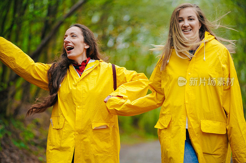 两个穿着雨衣的女性朋友在雾霾的森林里在雨中奔跑