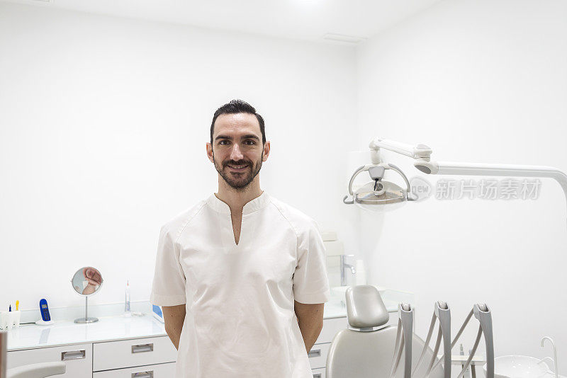 一个微笑的男医生在牙医办公室摆姿势的肖像