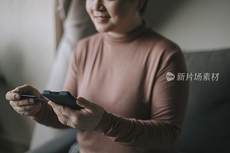 一位亚洲华人中年妇女用她的手机和信用卡在网上购物