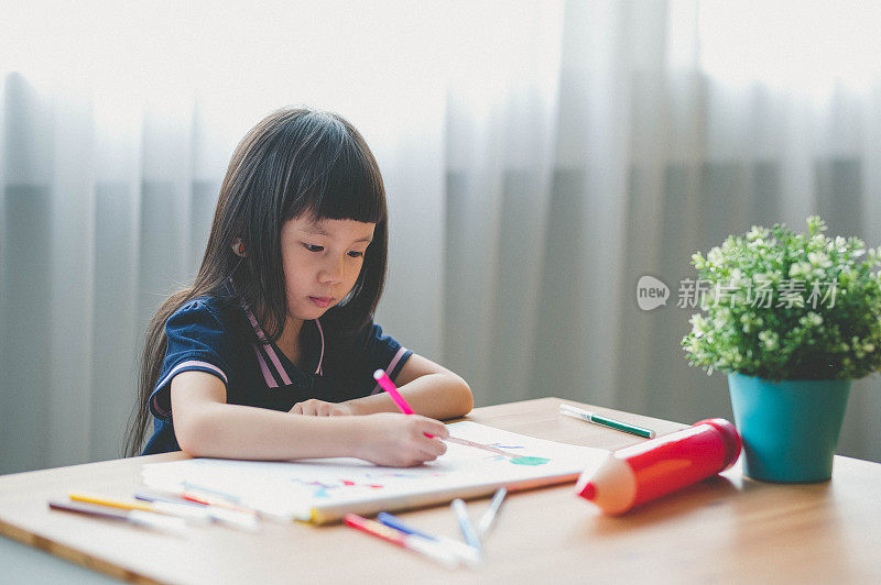 甜美的亚洲小女孩坐在桌子上，用彩笔在客厅画画