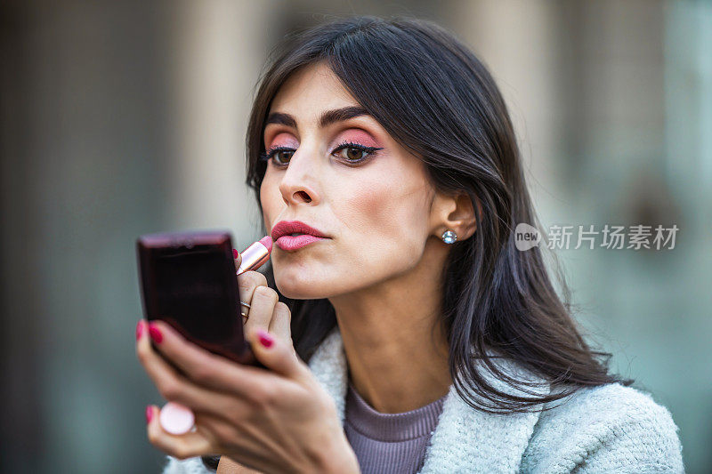 美丽的中年妇女拿着红唇和快速化妆在城市的街道上