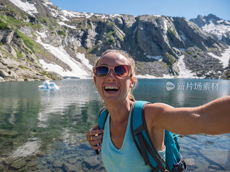 年轻女子在美丽的高山湖周围徒步旅行时自拍