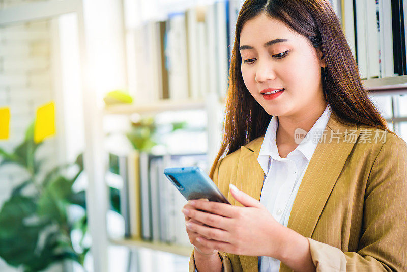年轻美丽的微笑亚洲女性使用智能手机或手机浏览或聊天在社交网络，互联网网络，放松的时间概念。