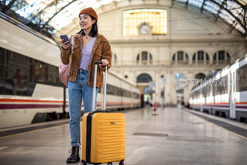 一位年轻美丽的中国女子在火车站等车时用手机，通过手机应用程序查看她的火车在哪个站台上