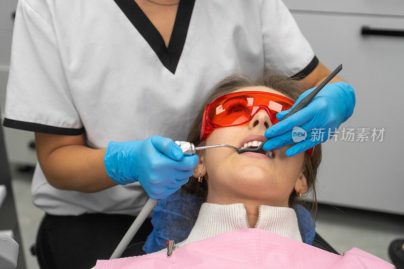 女牙医在口腔检查期间为病人洗牙。一名年轻女子戴着安全眼镜坐在牙科椅上看牙医。