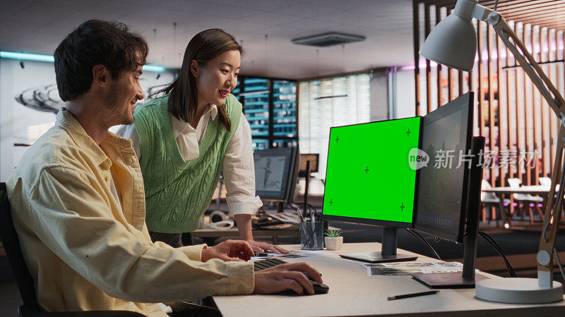在游戏开发工作室办公室，白人男性游戏设计师使用绿屏台式电脑与亚洲女性项目经理交谈。不同的同事讨论新的RPG游戏