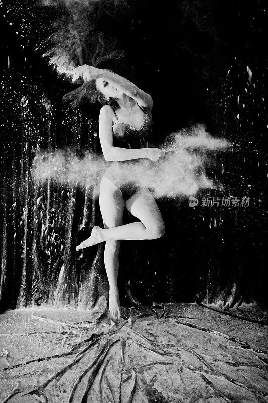 女孩舞者在白色的灰尘和面粉在黑色的背景跳舞。一名女子在面粉上跳舞。