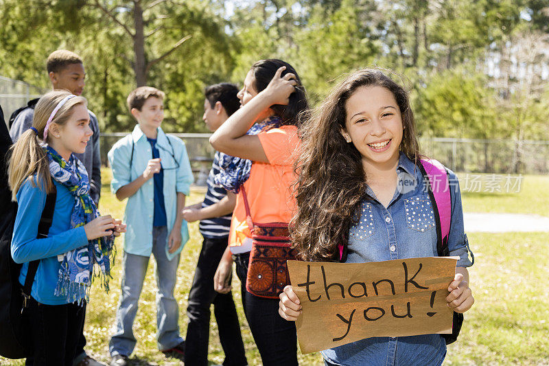青少年:拉丁女孩拿着“谢谢”的牌子。群的朋友。