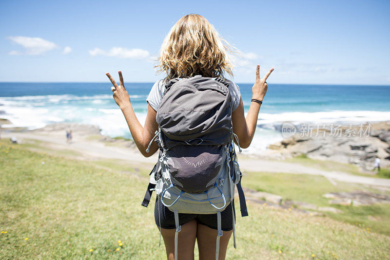 女性独自背包旅行者在海滩做和平手势