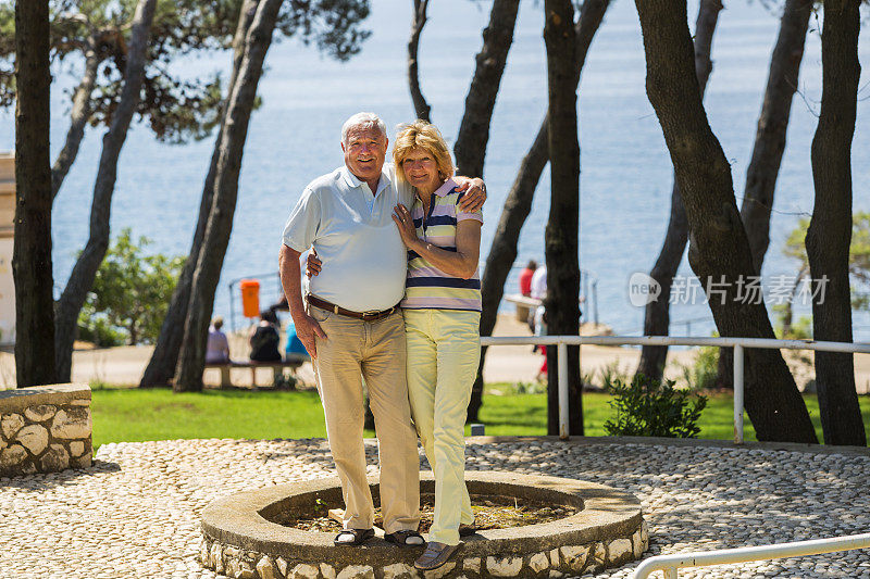 老年夫妇在海边的酒店公园里拥抱....