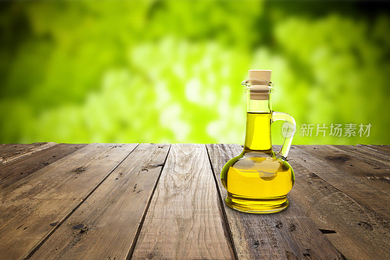 木质桌子上放着橄榄油瓶，背景是繁茂的树叶