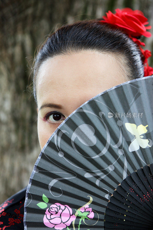 年轻的亚洲妇女穿着中国服装用扇子遮住脸
