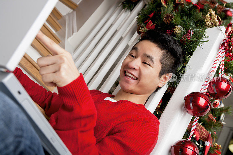 圣诞微笑的亚洲人指着笔记本电脑