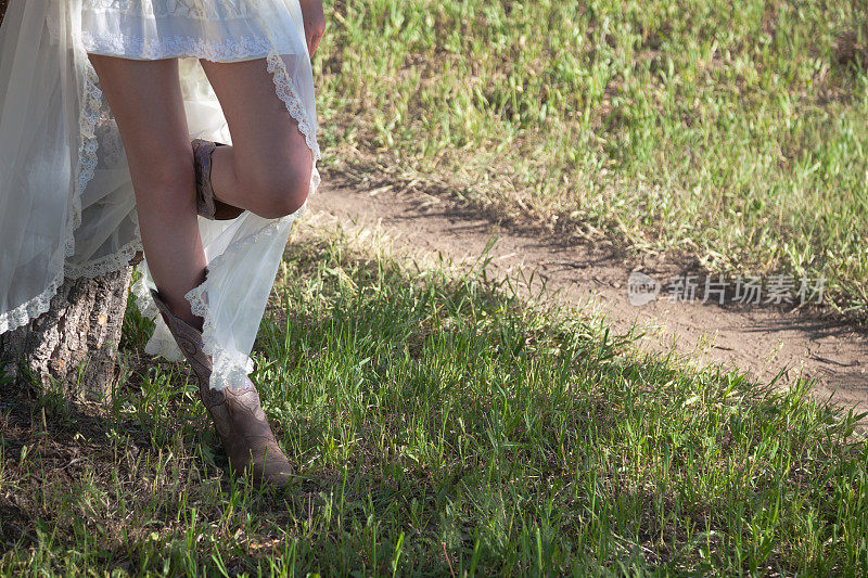 新娘穿着牛仔靴走在阳光明媚的草地上