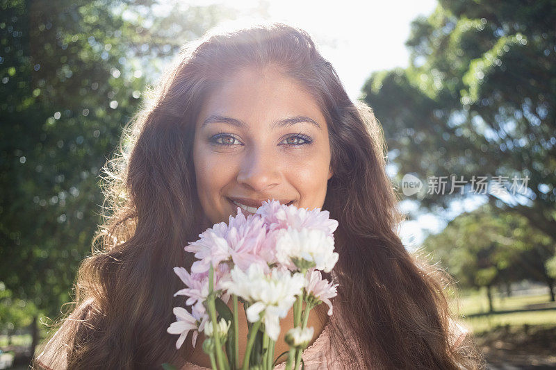 美丽的黑发女子在公园里闻着花香