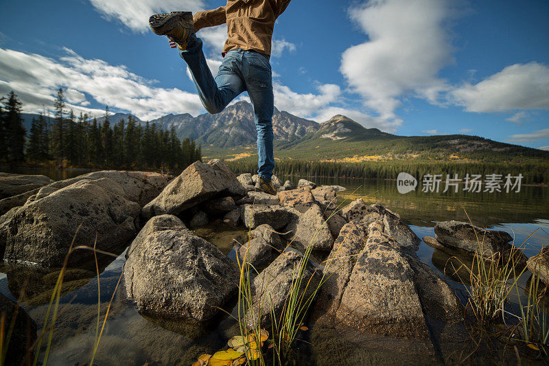 徒步者在山上的湖里跳岩石到岩石。低角度的观点。