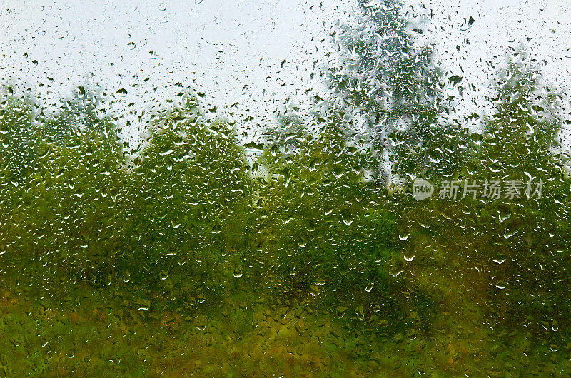 景观和多云的天空透过水滴雨潮湿的窗户