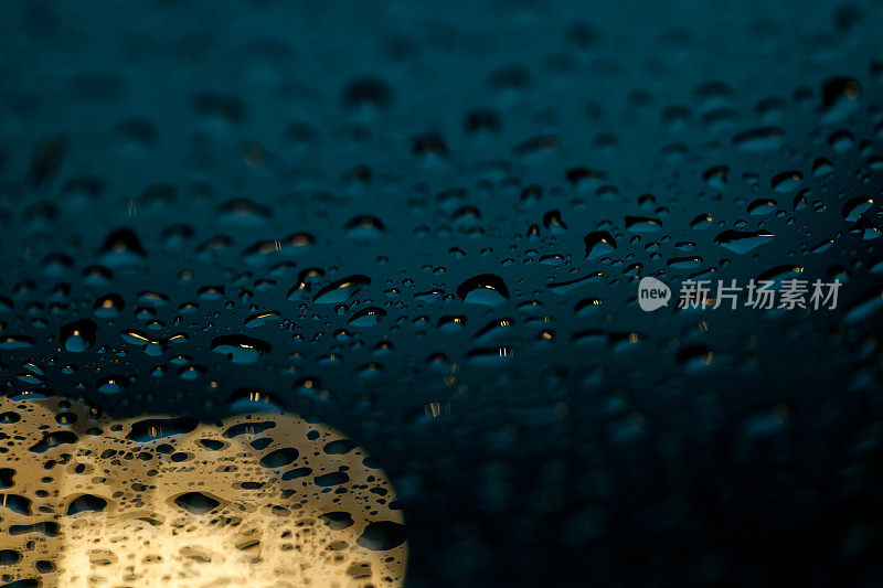 雨点落在挡风玻璃上，车头灯在背景中