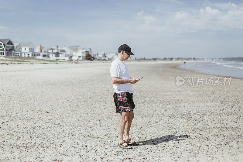 一个在海滩上看手机的成熟男人的肖像