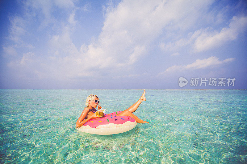 一个金发女人在马尔代夫的海上漂浮在充气甜甜圈上