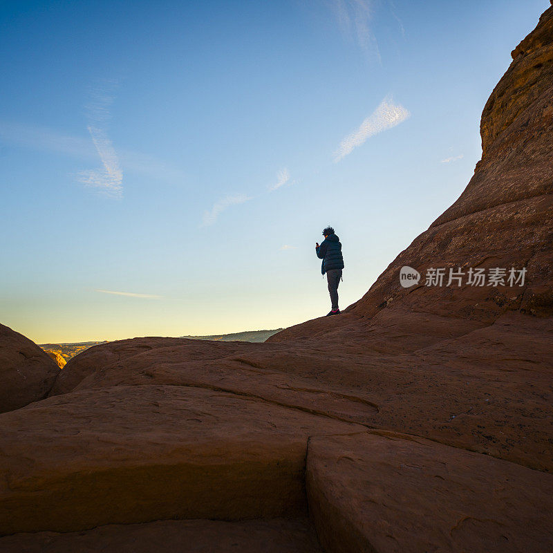 这位年轻的潮人、旅行者和徒步旅行者在犹他州精致拱门附近的红色峡谷里欣赏日出