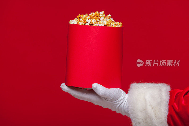 圣诞节。圣诞老人戴着手套的手与一个红色的桶爆米花，在红色的背景