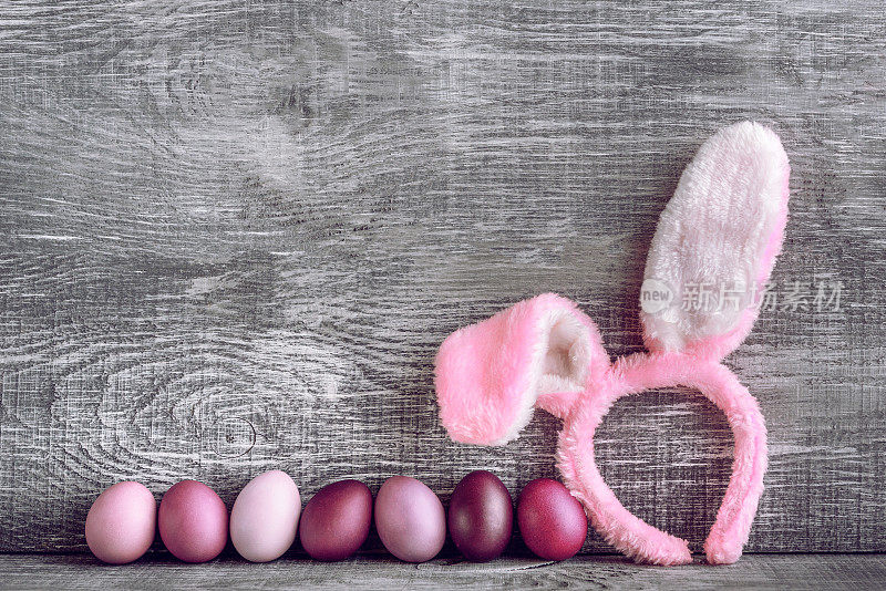 复活节彩蛋在一个时尚的颜色，在一个灰色的木制背景与一个女环与复活节兔子耳朵