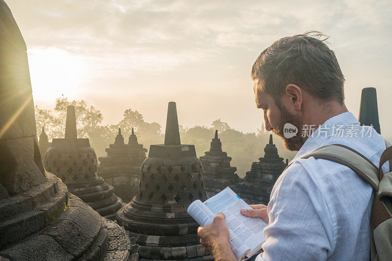 在印度尼西亚的婆罗浮屠寺，一个正在亚洲旅行的年轻人正在阅读导游书