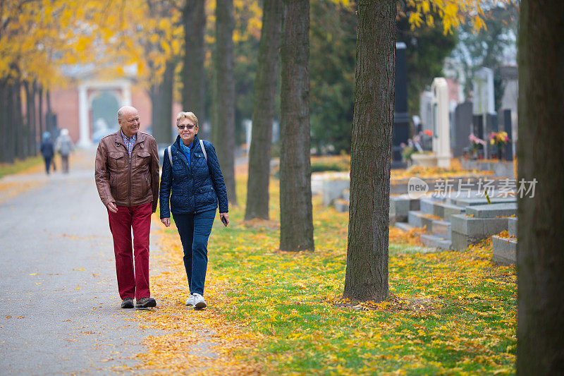 老年人对世界-微笑活跃的老年夫妇走过墓地在秋天