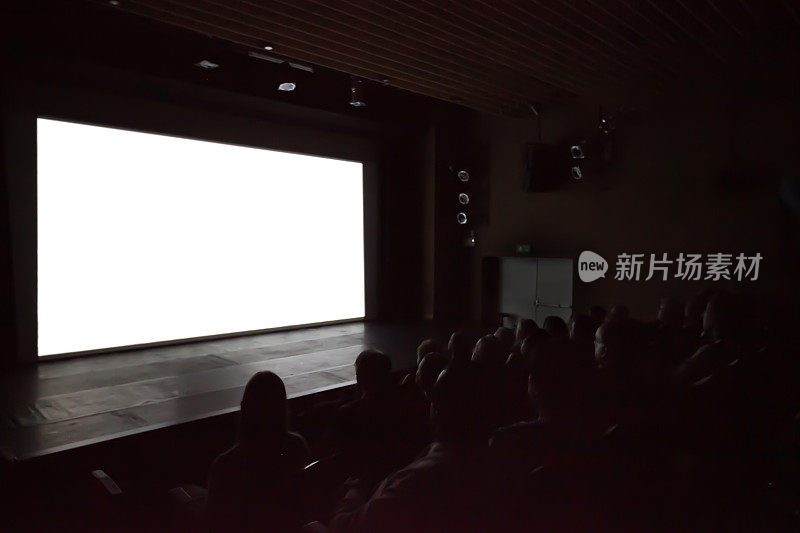 背景模糊的人看电影在电影院的白色屏幕。