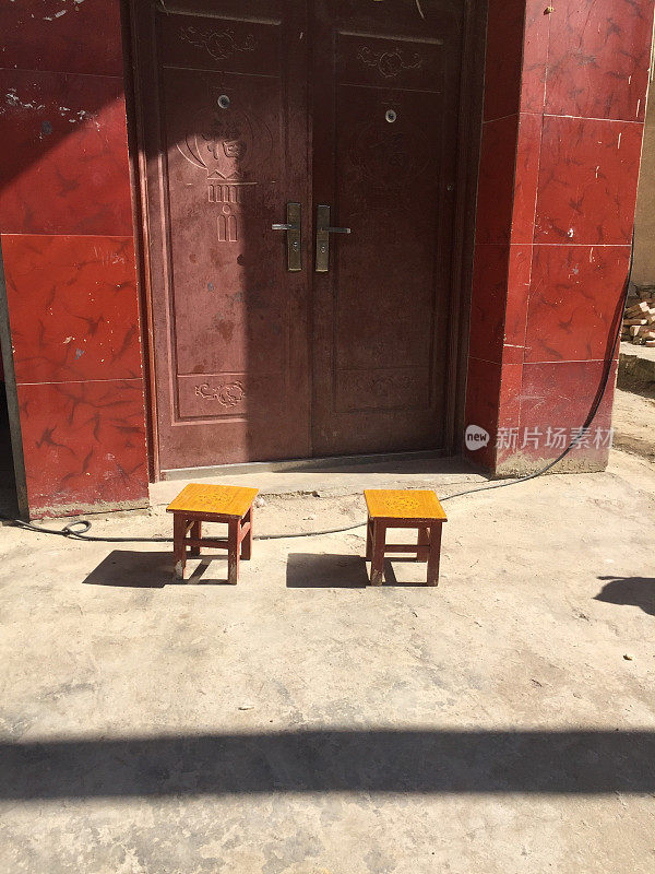 一对木凳在一扇红门前的街道上(中国云南)