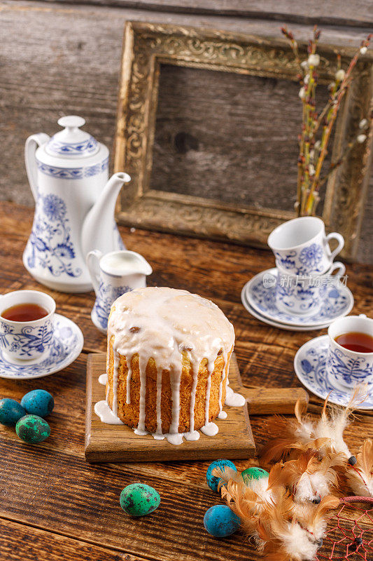 复活节的节日茶会为节日装饰的桌子。自制美味的糖霜蛋糕和染色的鸡蛋。背景中的一个古老的画框。