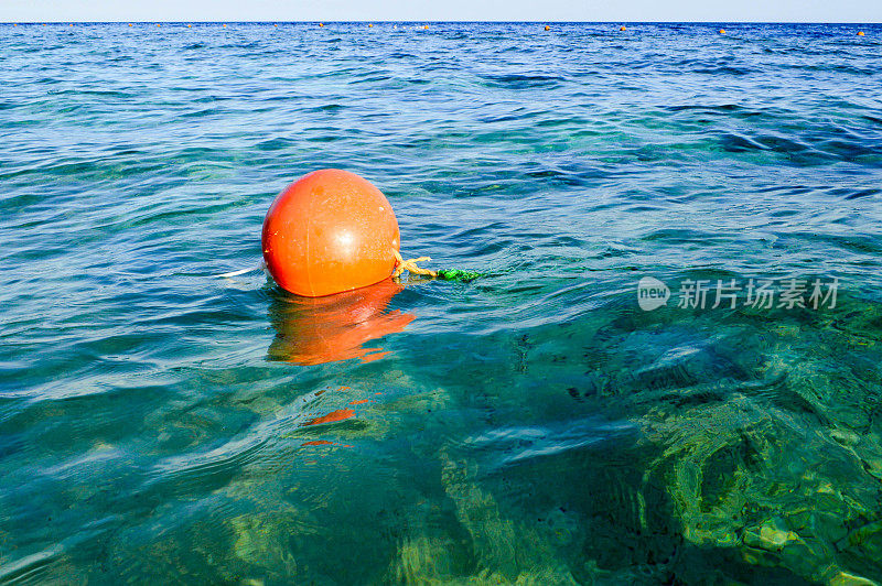 橙色的大型圆形塑料充气救生灯塔，浮标漂浮在蓝色的盐海中，以保证安全