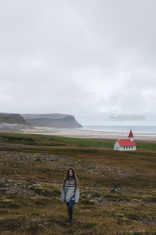 穿着羊毛衫的女人跑到遥远的美丽的教堂附近的海洋和山脉在冰岛