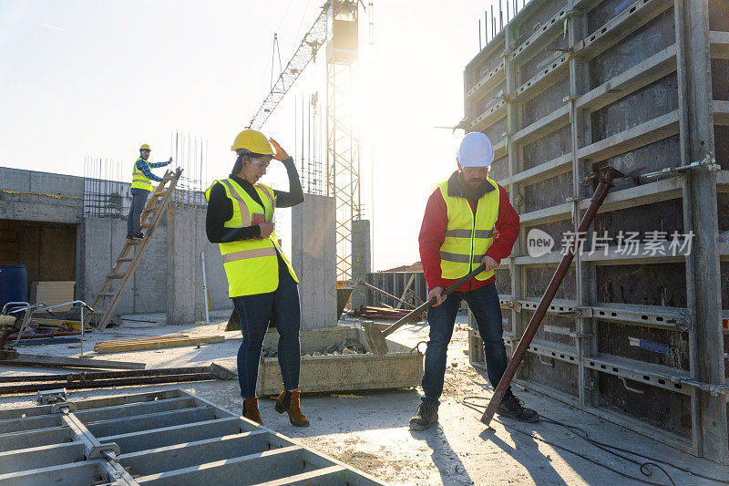 一个阳光明媚的日子，一位自信的女建筑师拿着平板电脑和一位建筑工人在一个住宅楼的工地上一起讨论和工作。