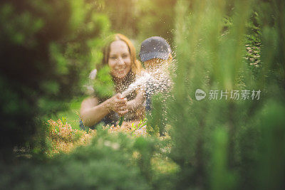 在阳光明媚的日子里，一名妇女和她的儿子在自家花园里浇水